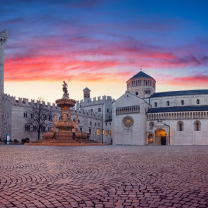 イタリア北部トレントのドゥオーモ広場。夕暮れの空の下、中世の建築と大聖堂が並ぶ歴史的な街並み