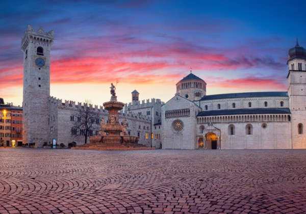 イタリア北部トレントのドゥオーモ広場。夕暮れの空の下、中世の建築と大聖堂が並ぶ歴史的な街並み